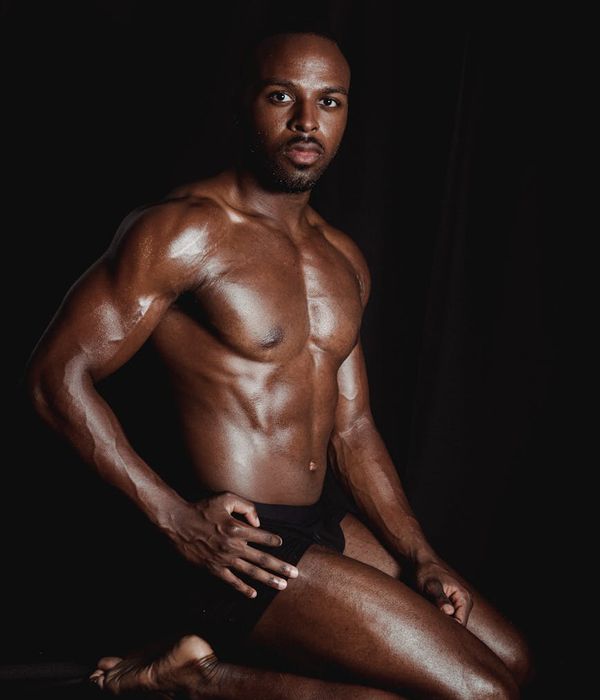 Masculine man performing stability and strength exercise in a dark studio.